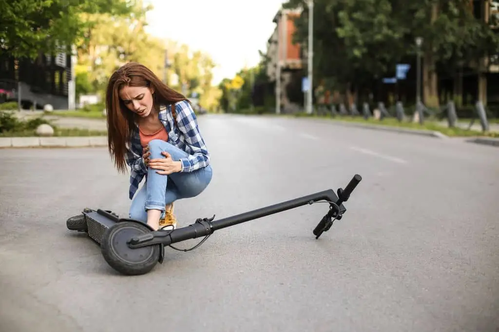 A woman holds her knee in pain after falling down while using an electric scooter.