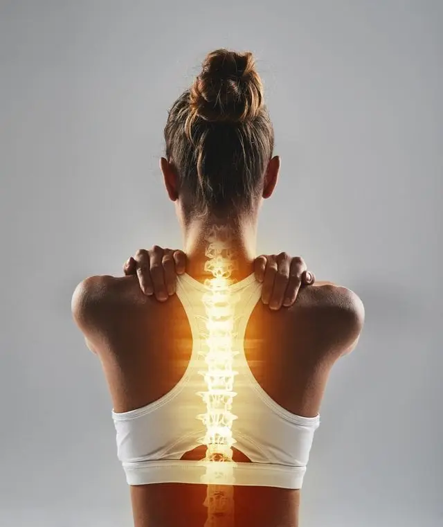 a woman facing away from the viewer has her hands on her shoulders. Her back has an illuminated graphic of a spinal cord. 