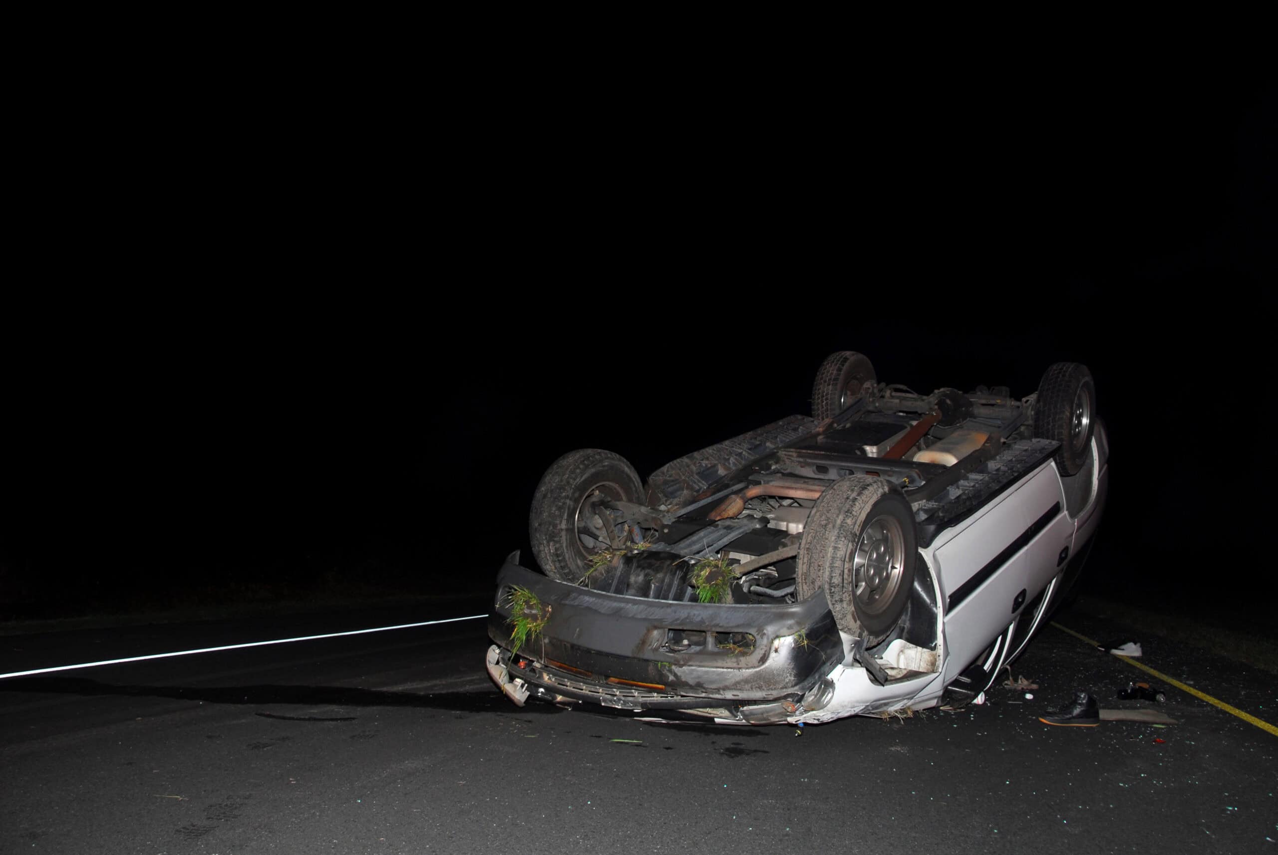 A vehicle turned upside down on its roof on a dark road after a rollover car accident