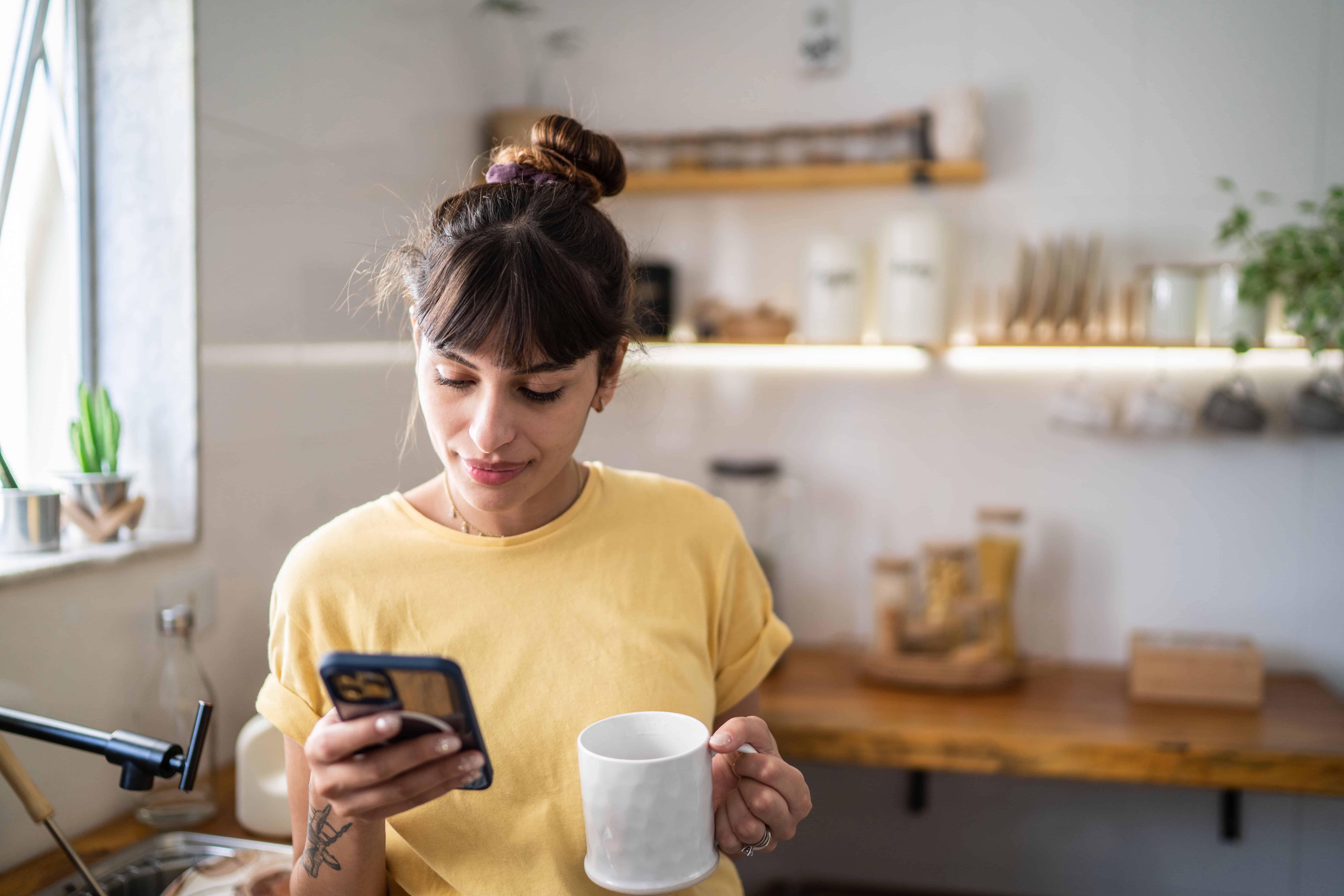 A woman enjoys a cup of coffee while scrolling through social media on her phone.