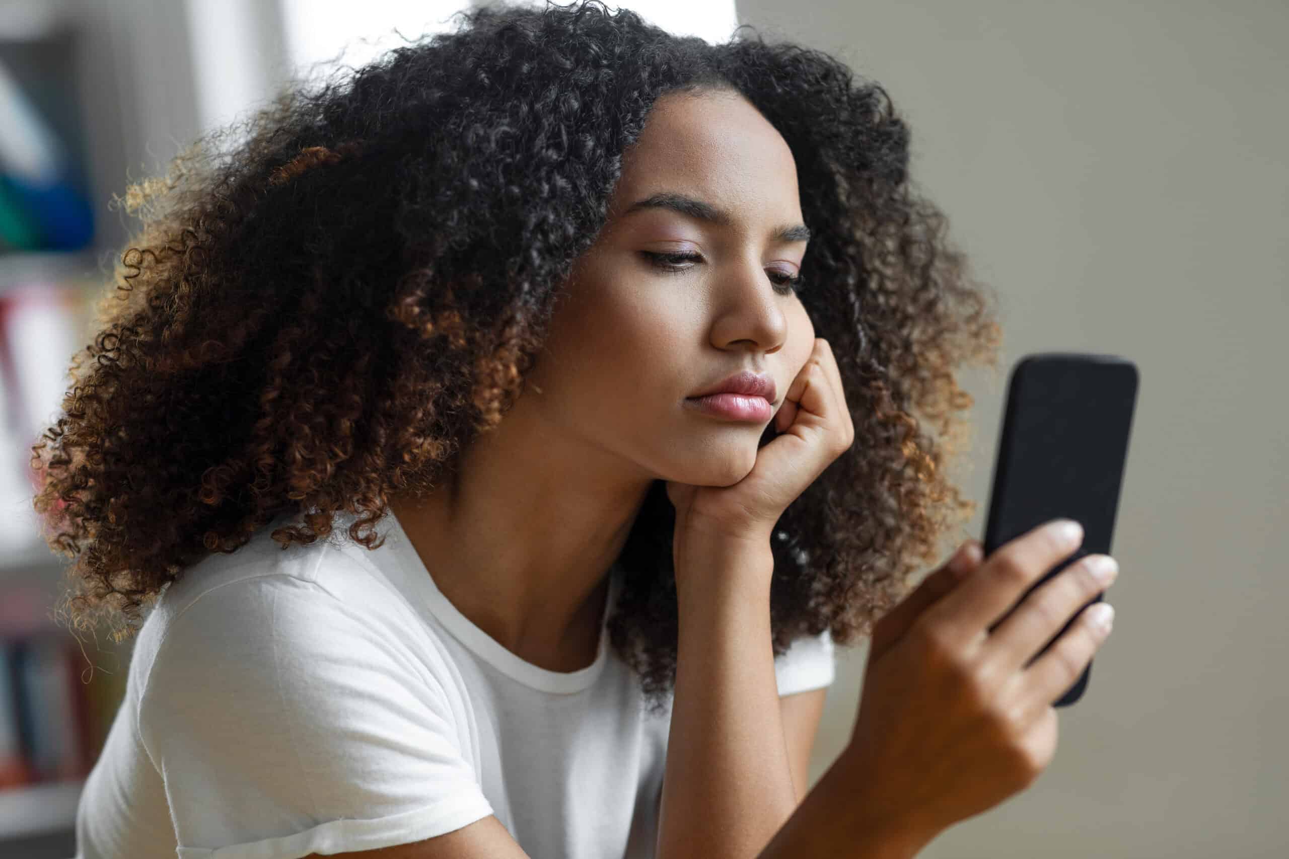 A woman looks at her phone, looking sad.
