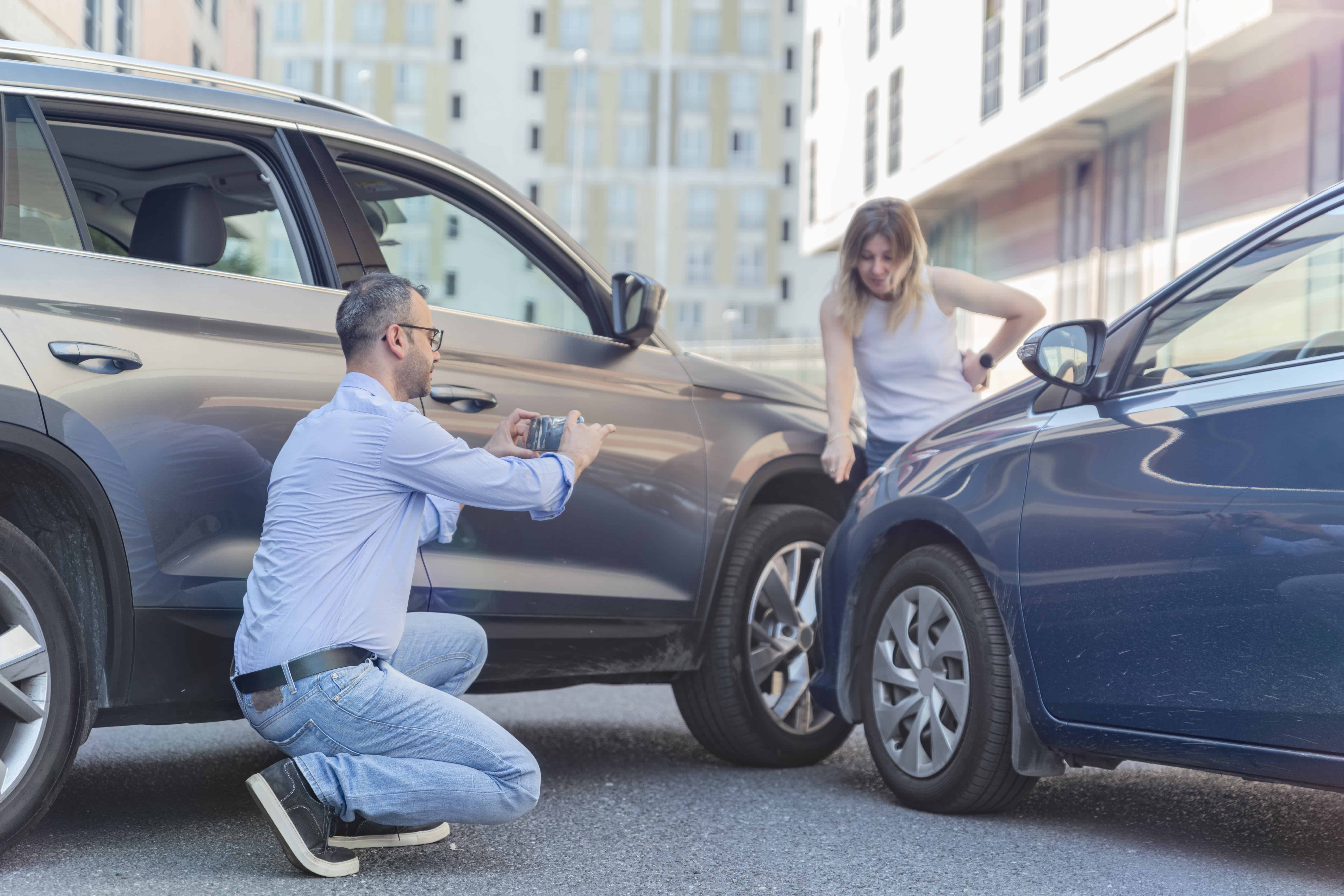 a man takes pictures for evidence after a car accident while a woman points out details to him.