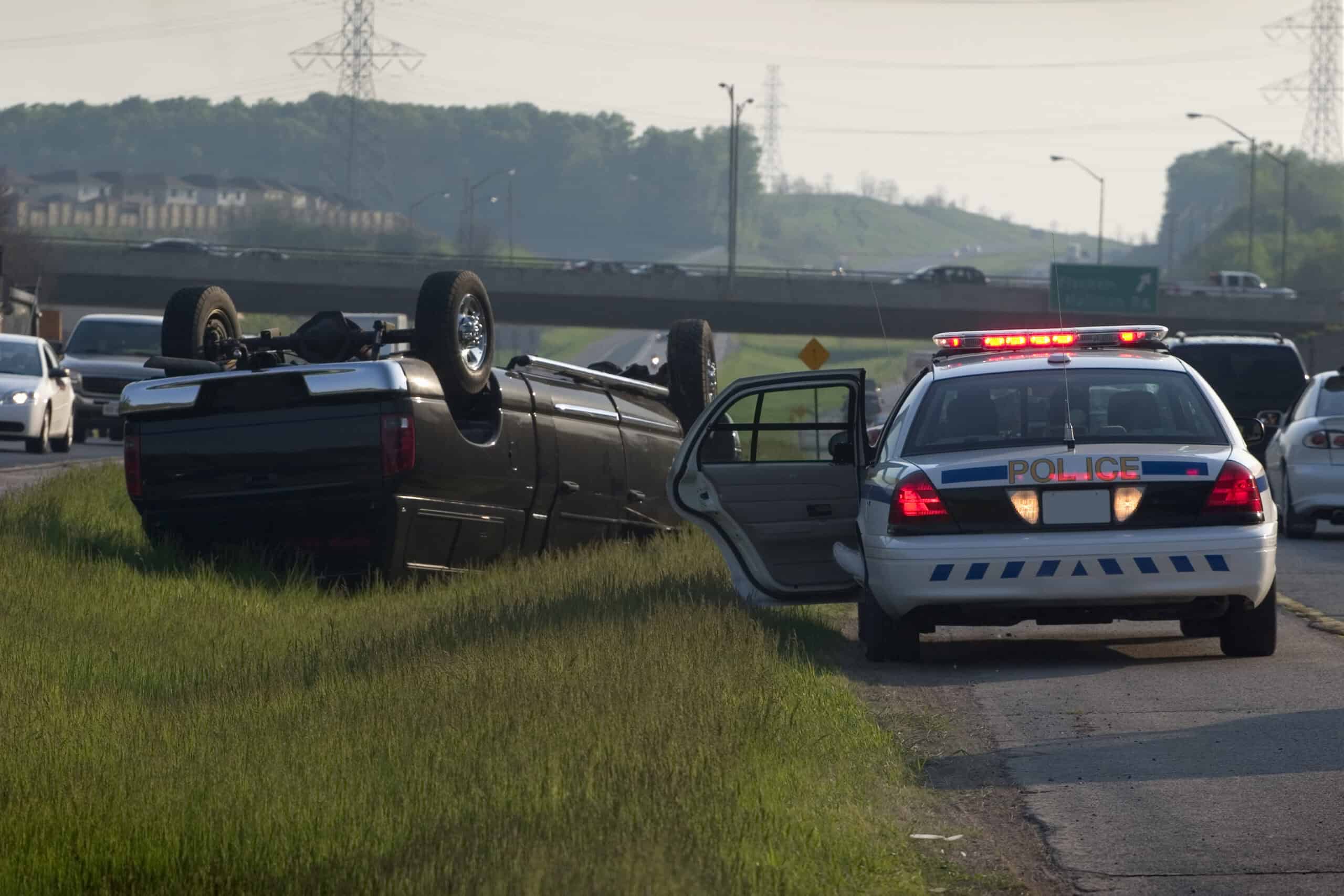 A large SUV rolled over in the middle of a busy median off of the highway. A police vehicle is on the scene.