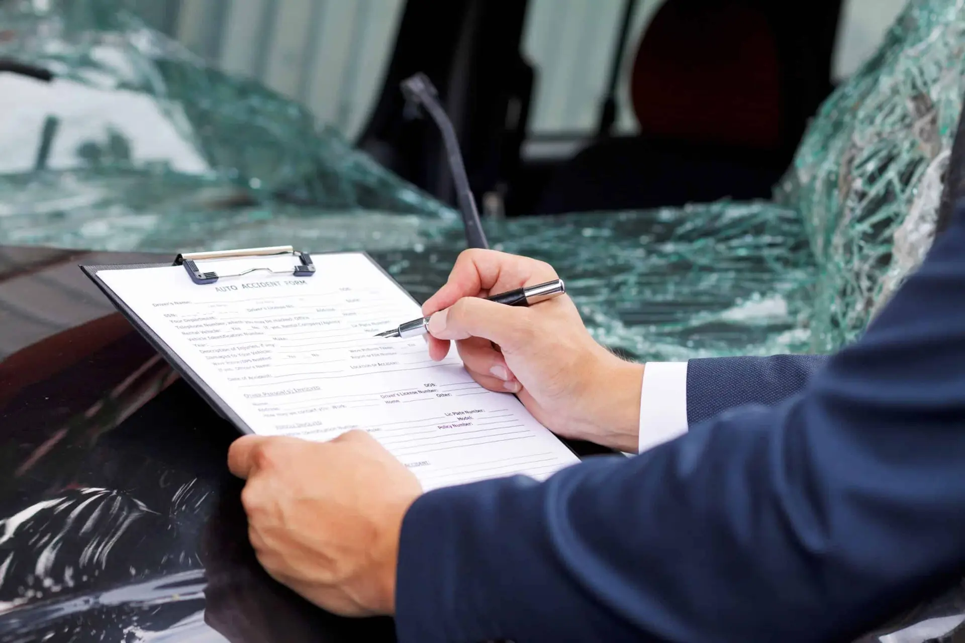An insurance adjuster takes notes on the damage done to a vehicle after a car crash.