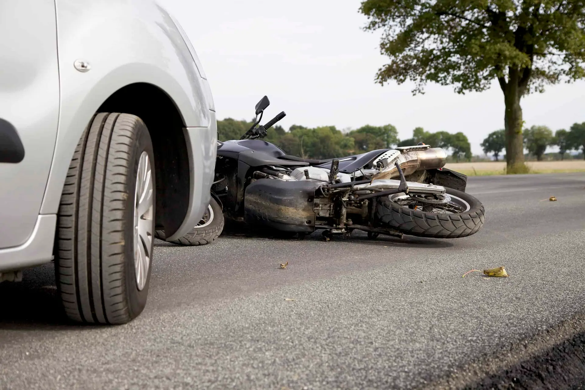 A motorcycle knocked to the ground in front of a car after an accident