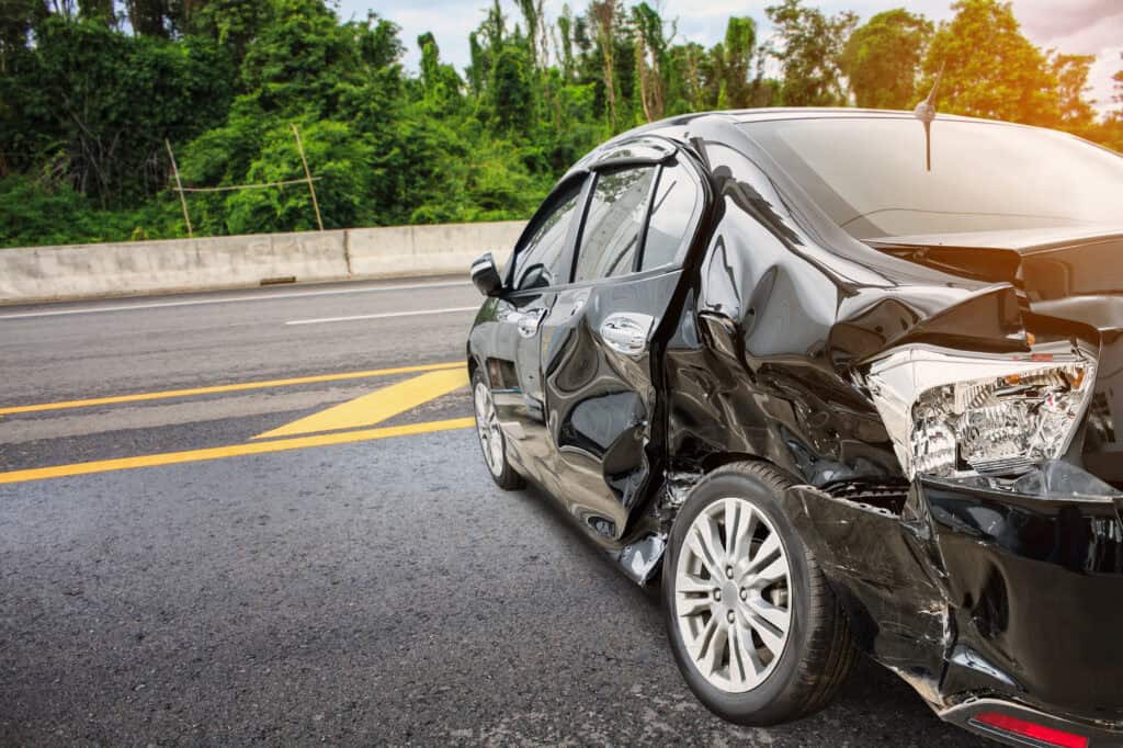 A black sedan with heavy damage to its side after being in an accident with a hit-and-run driver.