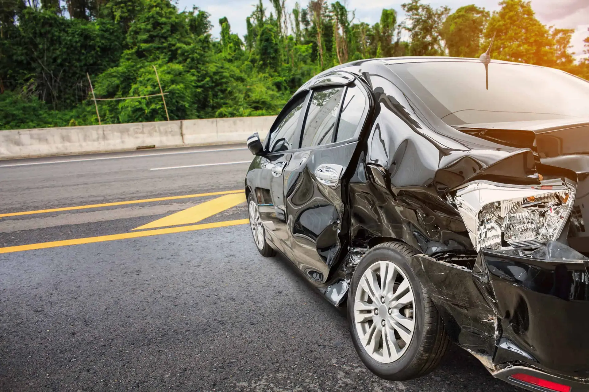 A black car with heavy damage to its side from a sideswipe accident occuring at high speeds.