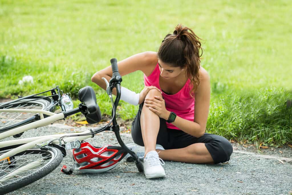 A woman is sitting on the ground and holds her knee after she was in a bicycle accident.