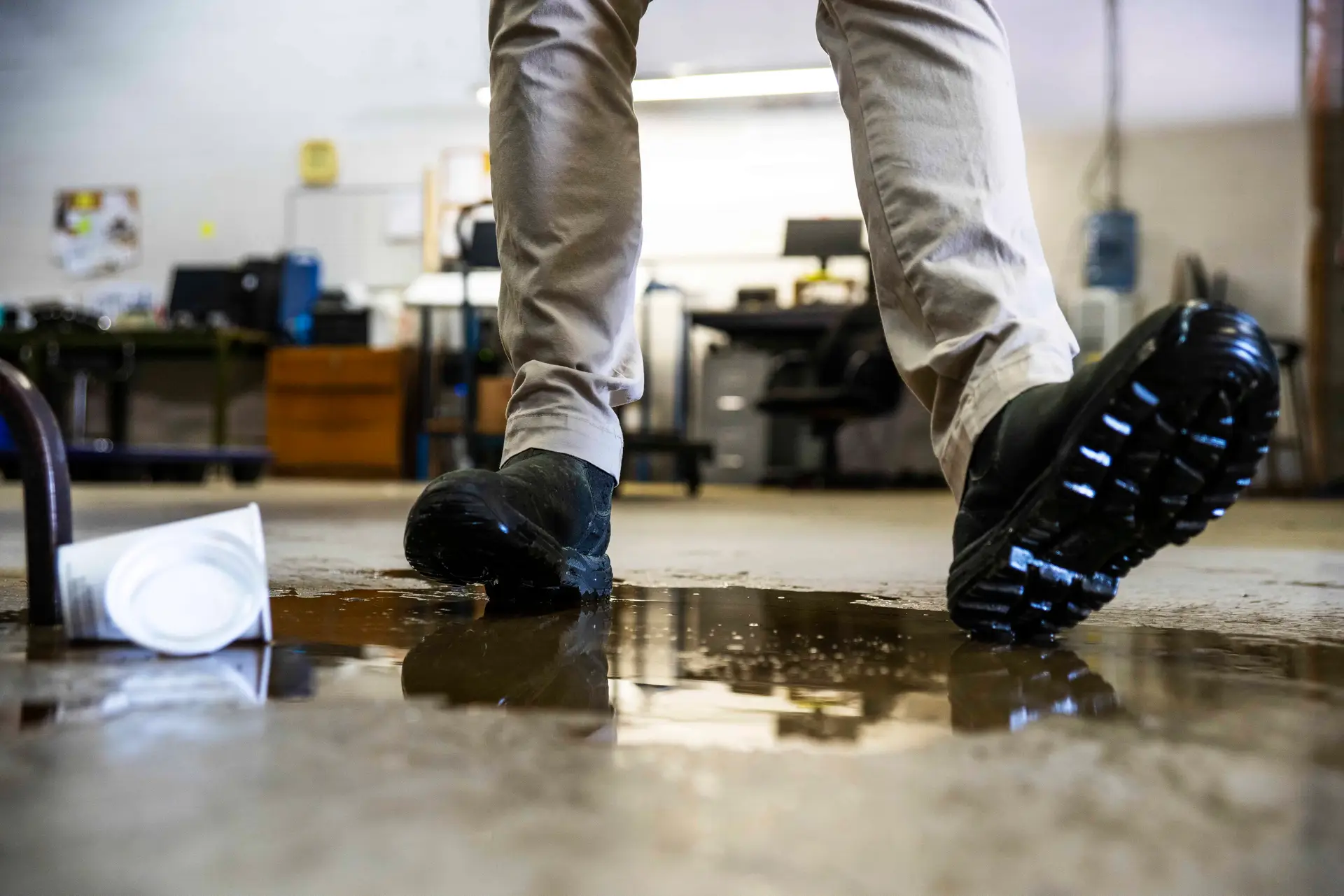 A person wearing boots loses their footing in a puddle of spilled coffee on the floor, leading to a slip and fall injury.