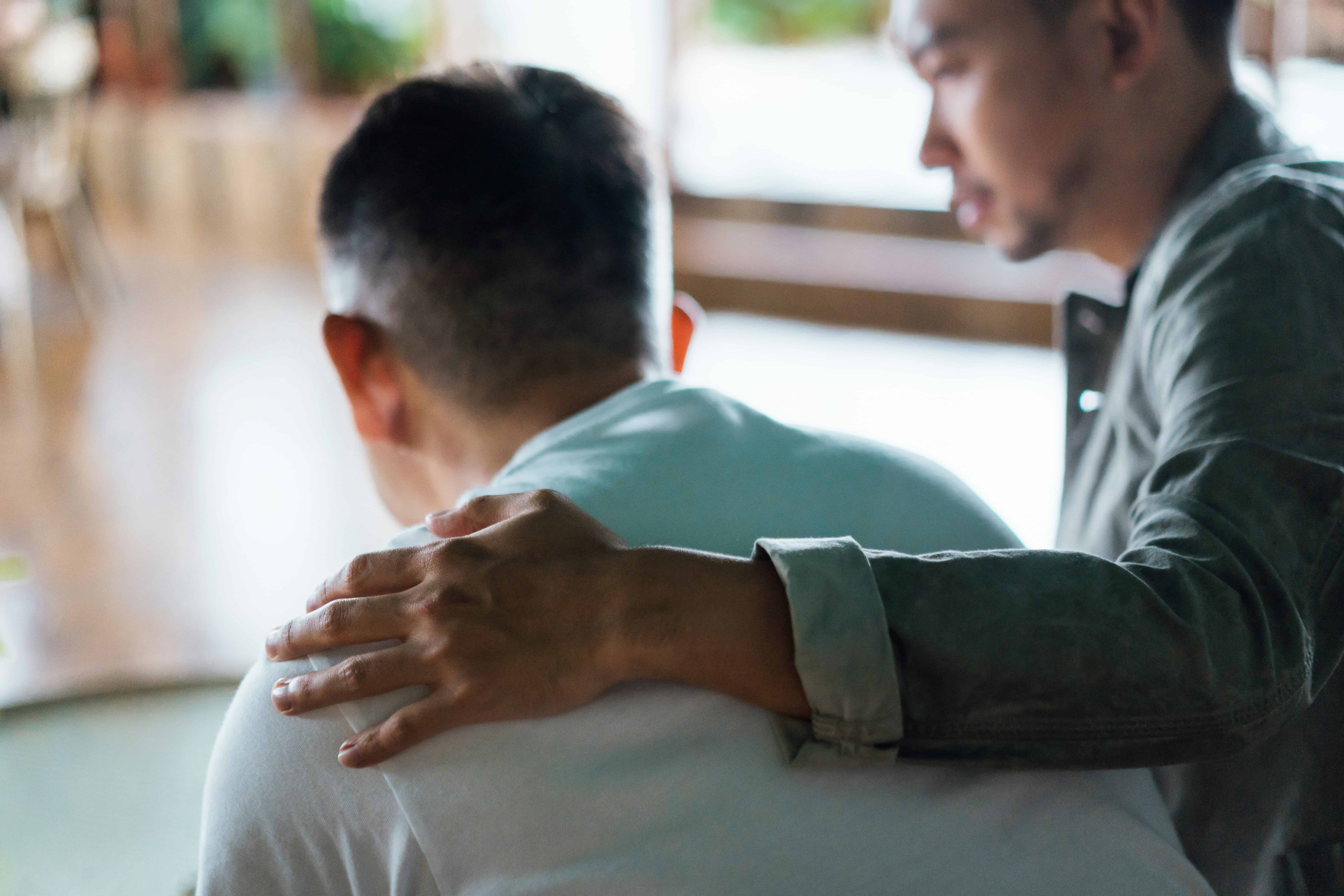 A man consoles another man at a funeral service for a deceased relative.