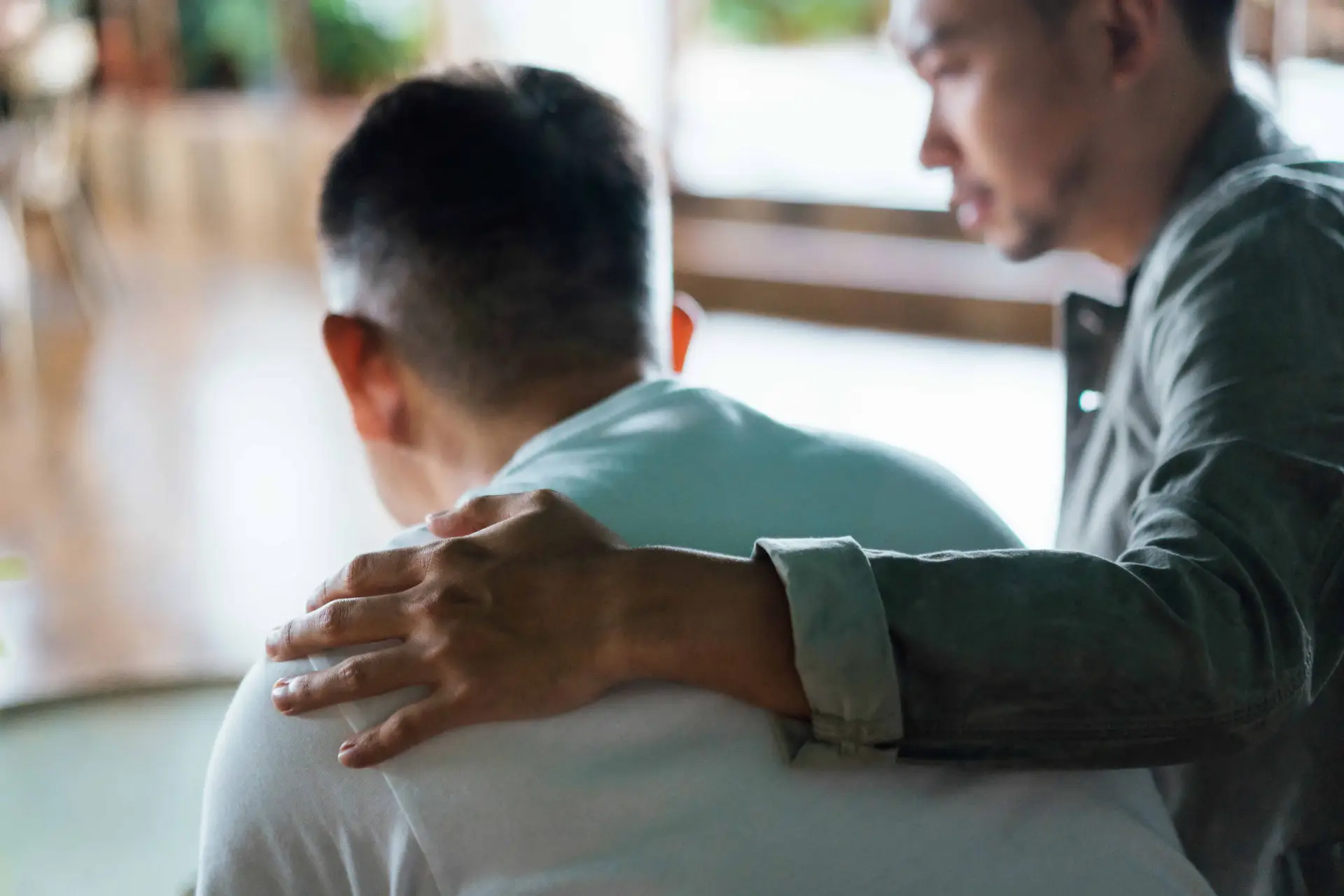 A man consoles another man at a funeral service for a deceased relative.