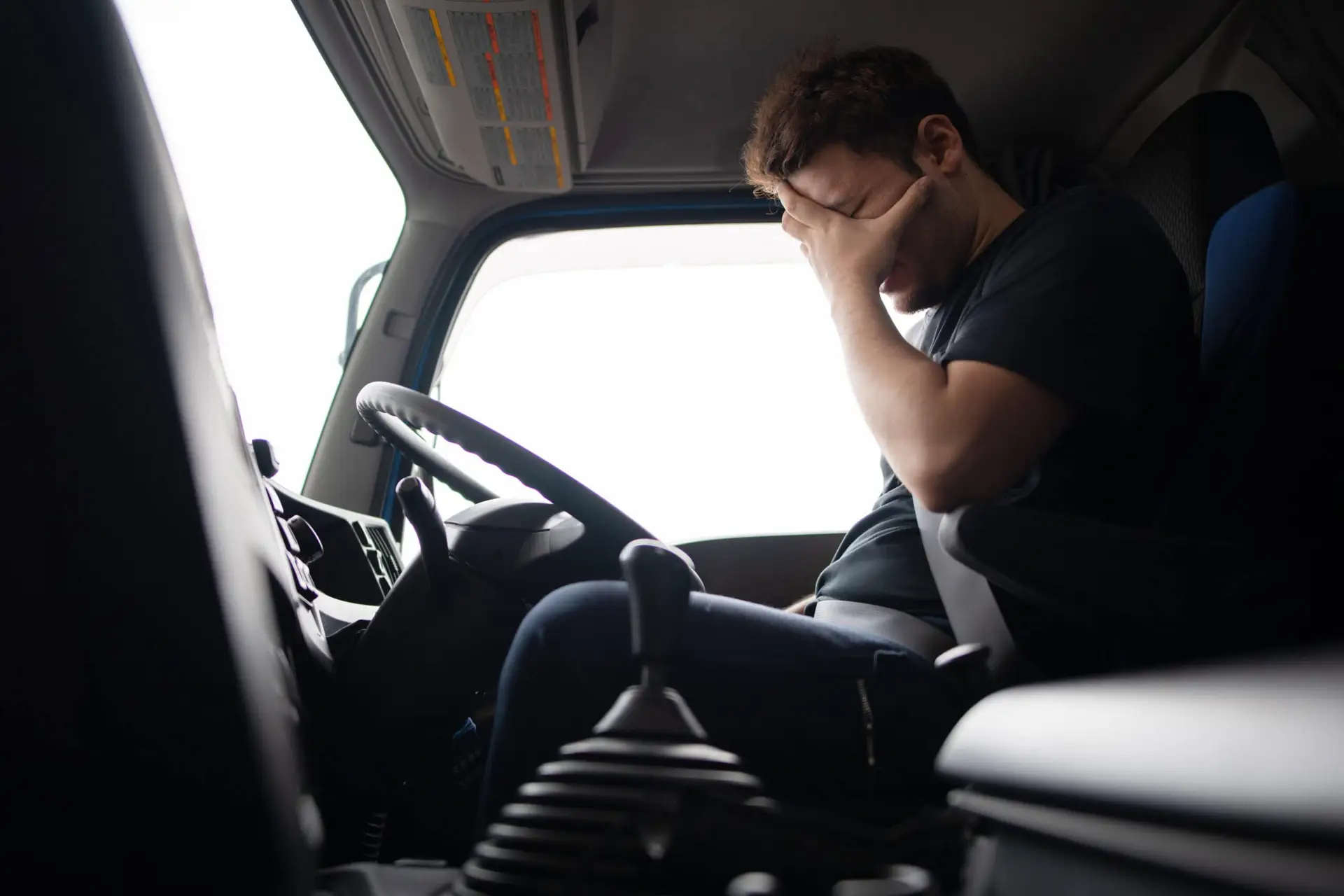 A fatigued truck driver rests his head in his hand while he is behind the wheel.