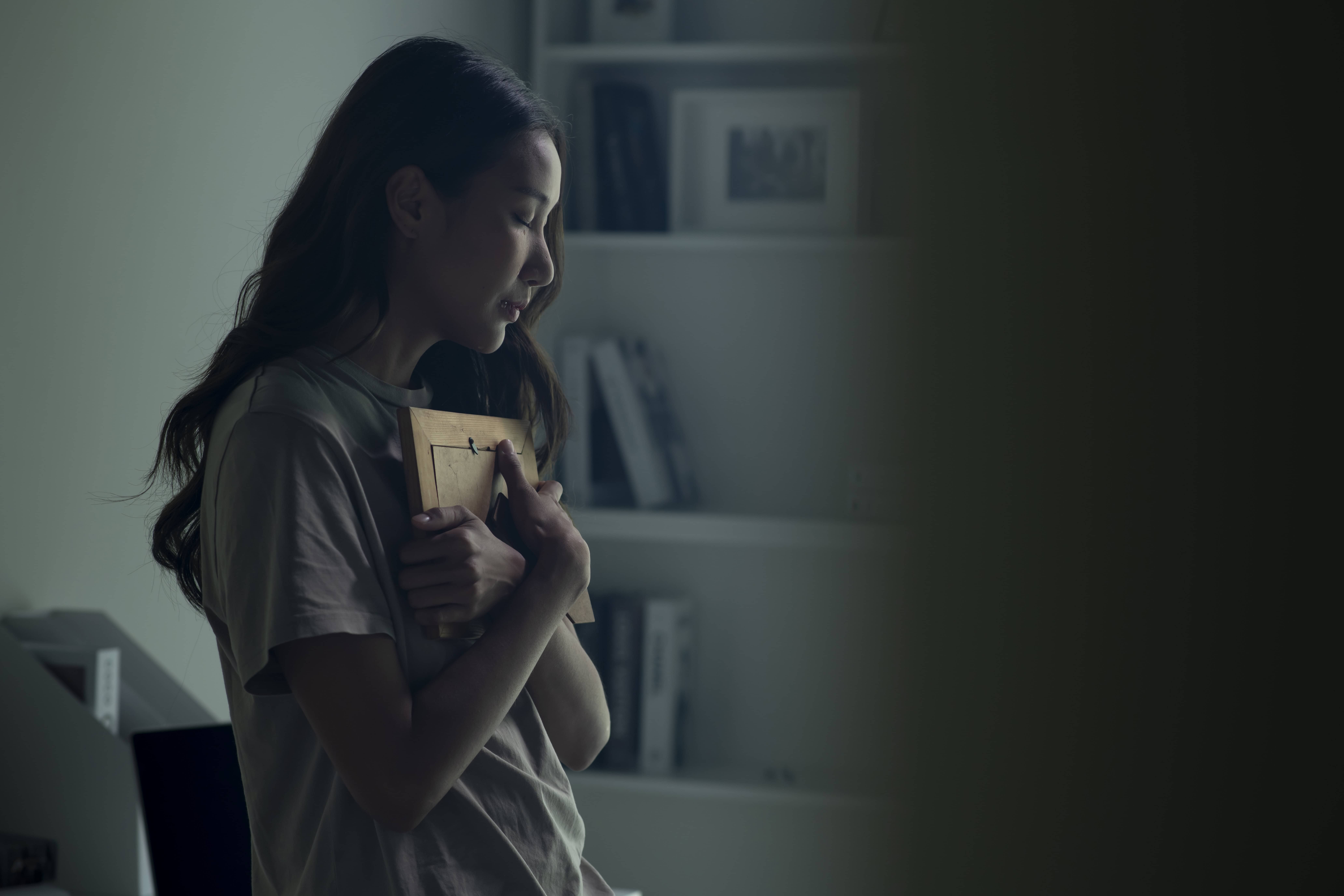 An upset woman cries while she holds a photo of a lost loved one close to her body.