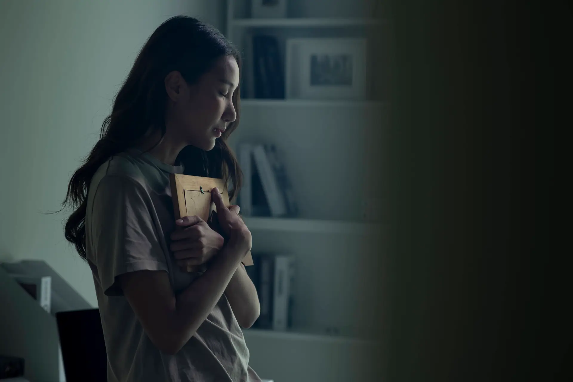 An upset woman cries while she holds a photo of a lost loved one close to her body.
