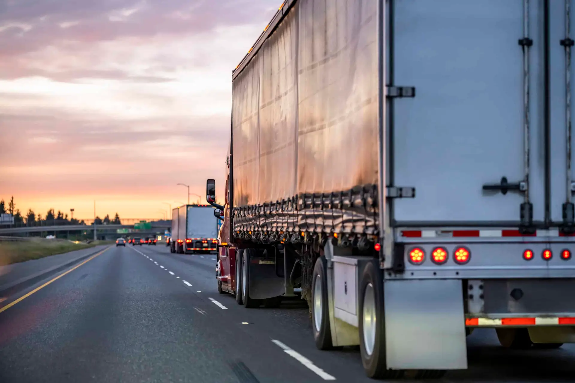A semi-truck traveling down an expressway at sunset. 