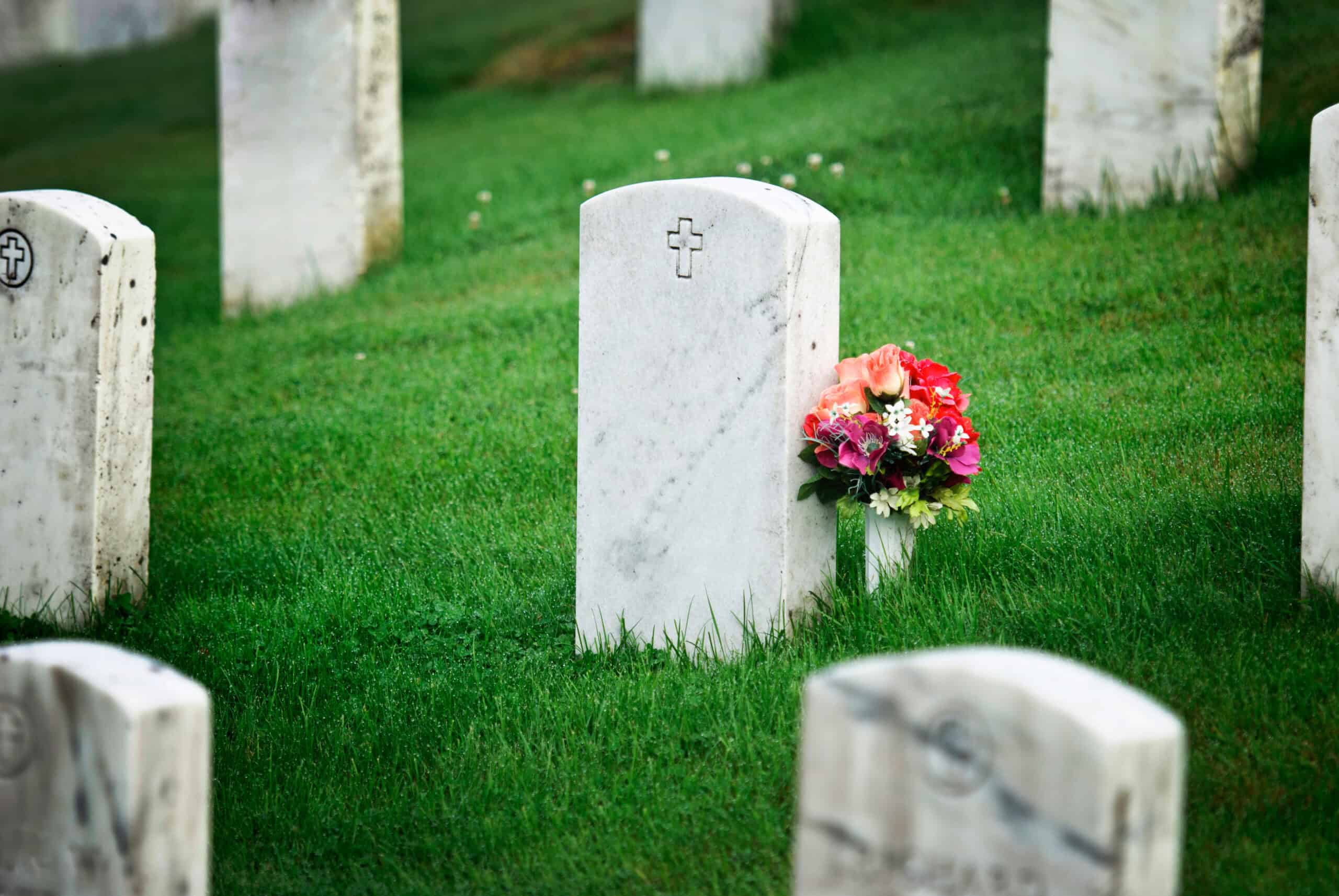 A gravestone in a cemetery with a bouquet of flowers next to it.