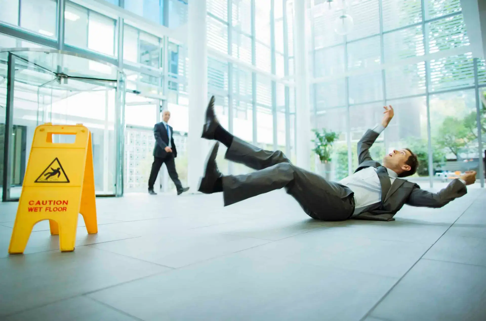 A man in a suit falls on a wet floor in an office complex.