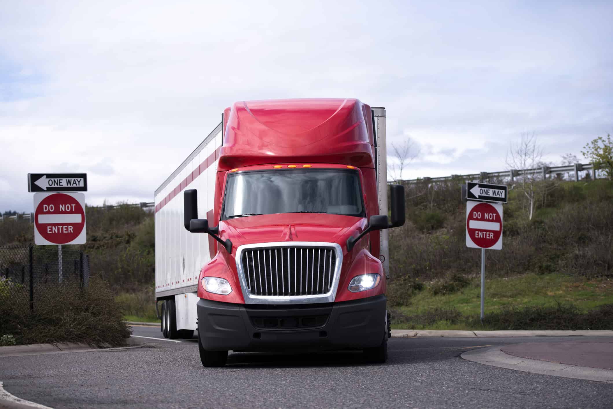 A large truck with a red cab makes a wide right-hand turn onto a road coming off of the expressway.