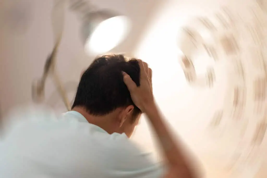 A man holds his head as the background appears to be spinning and blurry, giving the illusion of experiencing dizziness and vertigo after suffering a TBI
