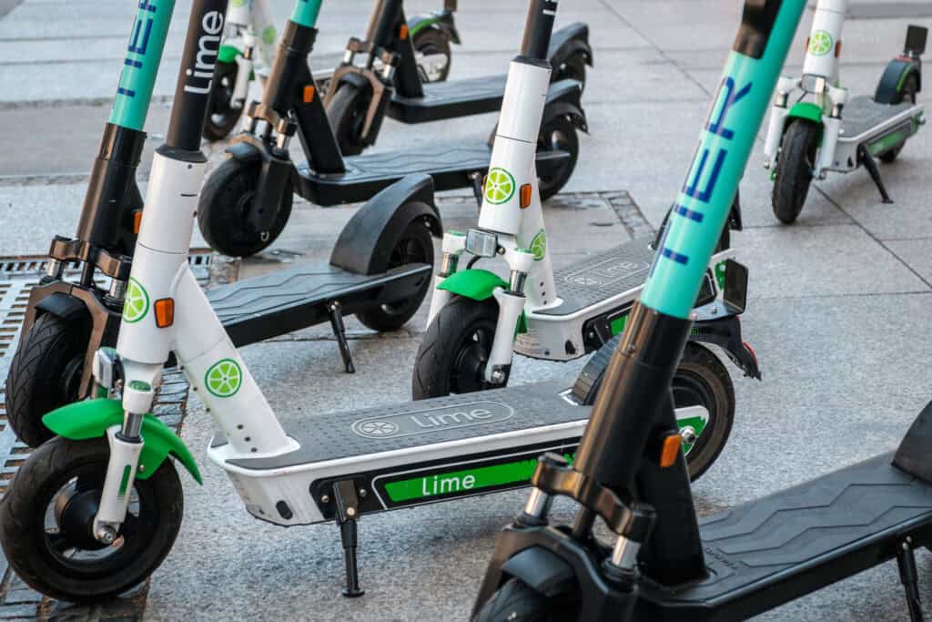 A group of Lime electric scooters parked on a sidewalk for use by customers who have downloaded the Lime App on their smartphones.