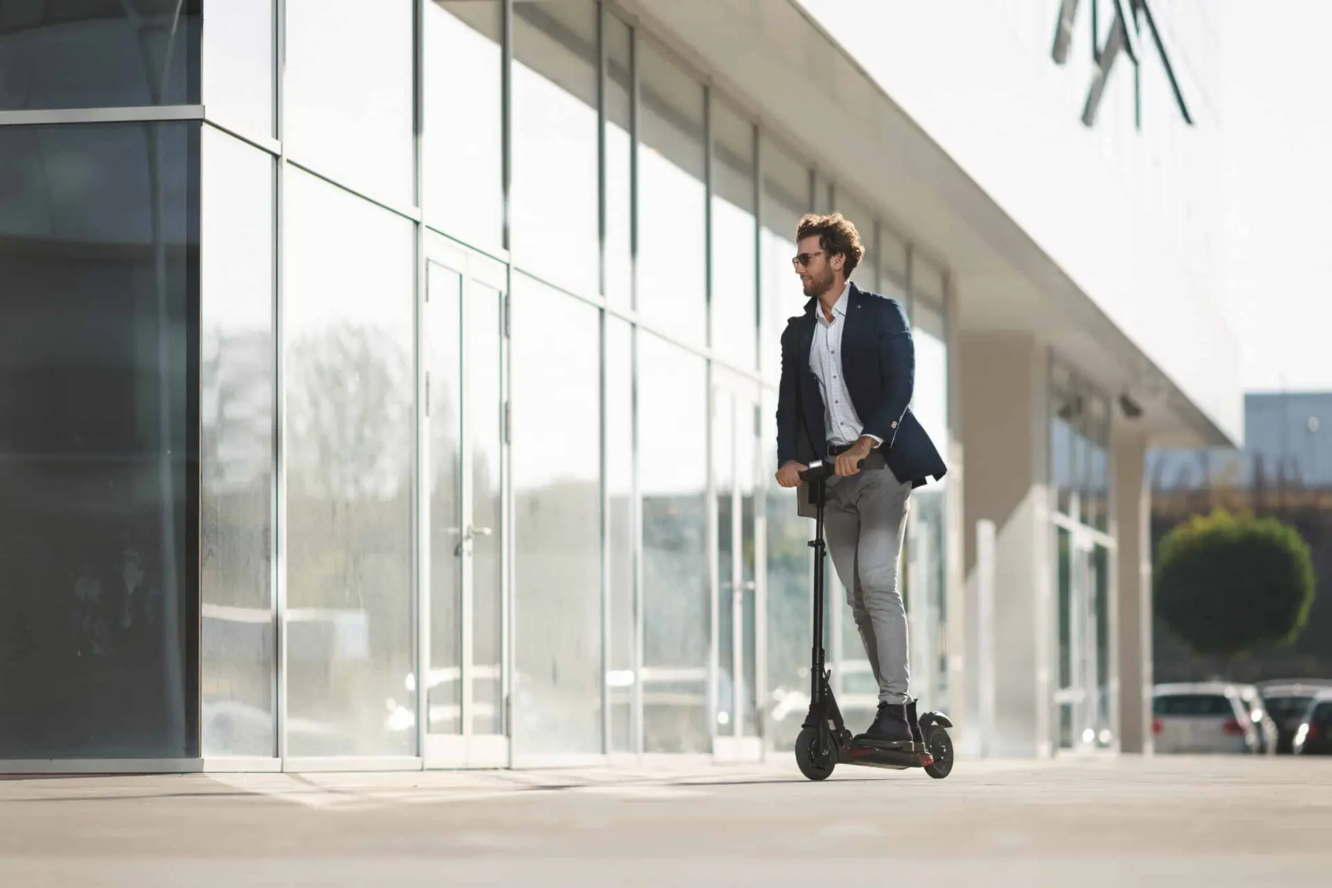 a man wearing business attire guides his electric scooter to his office complex.
