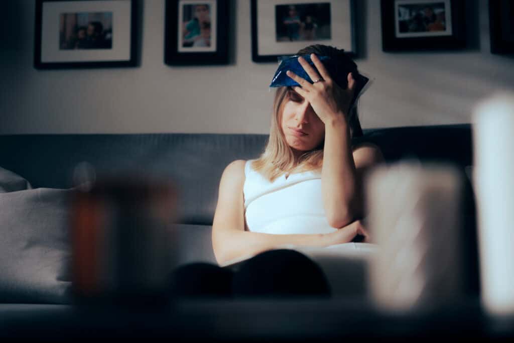 A woman leans back on her couch and holds an icepack to her head, trying to relieve pain from a head injury.