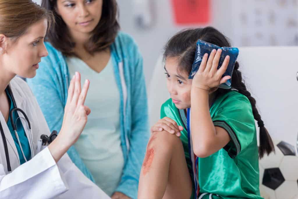 A doctor holds up fingers in front of a young female patient to assess her cognitive abilities to determine a traumatic brain injury treatment plan.