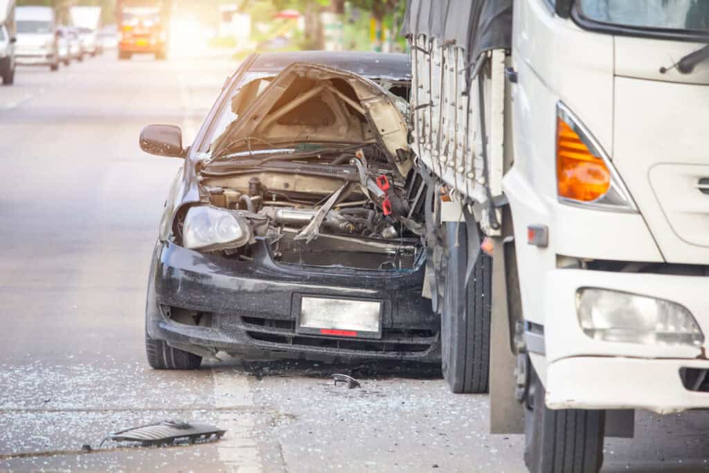 A heavily damaged black car after a fatal accident with a large, white delivery truck.