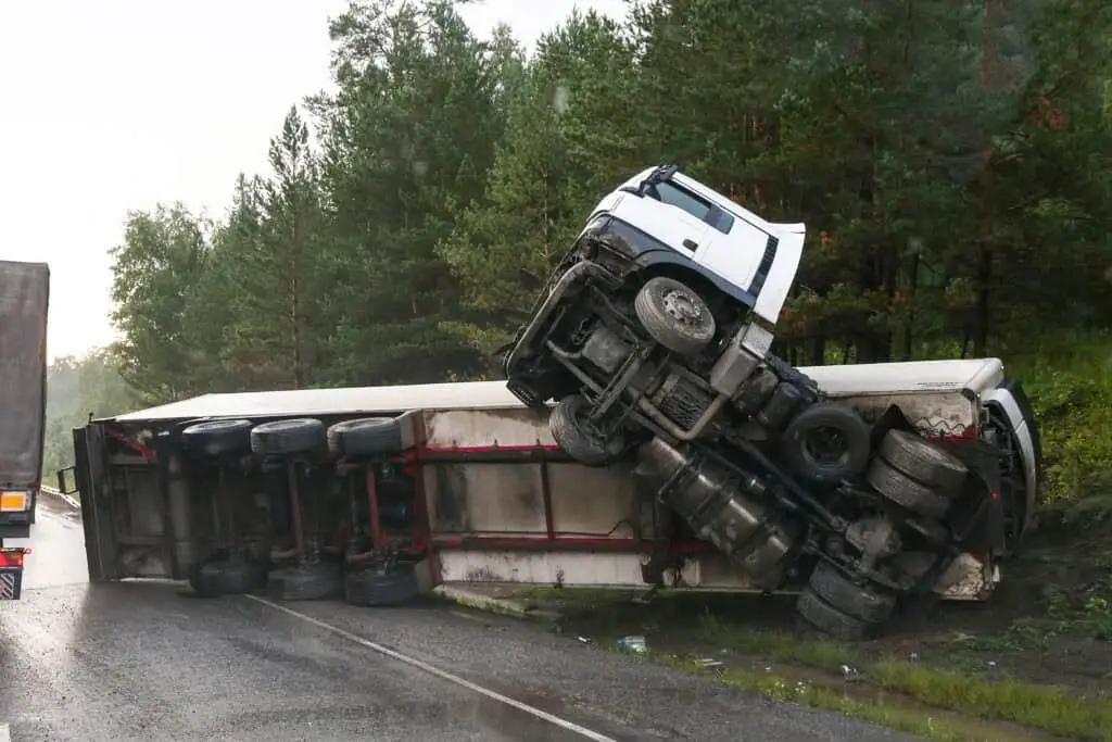A commercial truck is turned over on the side of the road after an accident.