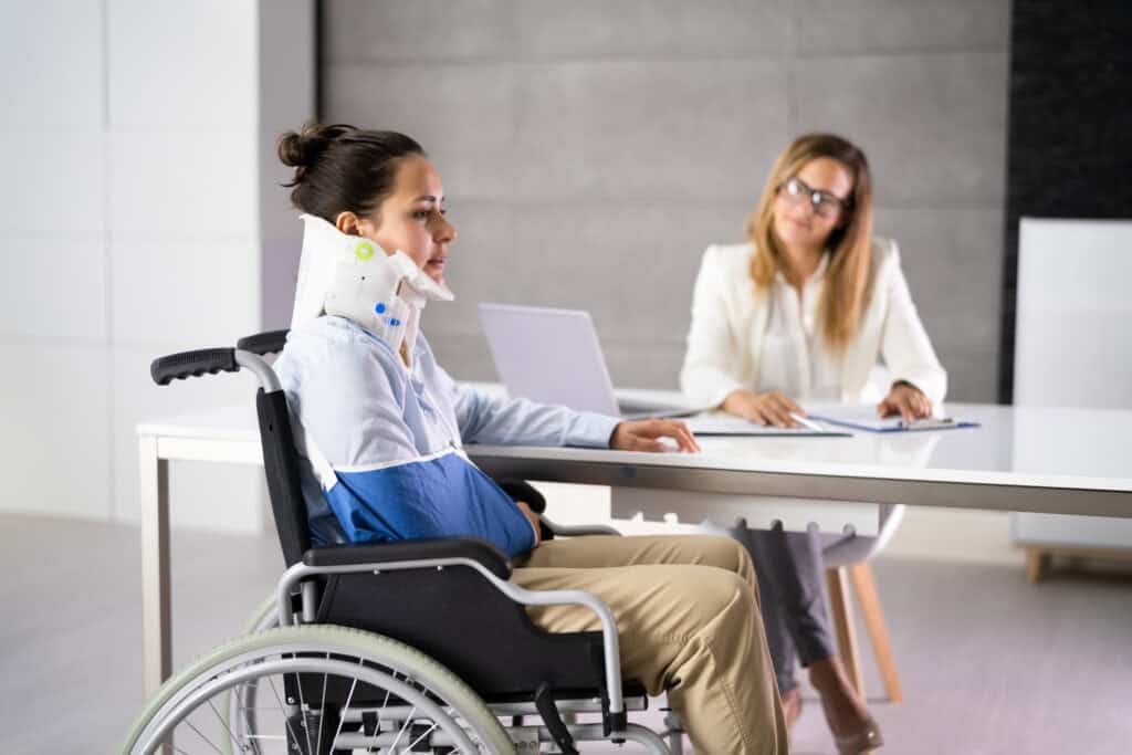 An injury victim that is in a neck brace and a wheelchair explains her case to her personal injury lawyer.