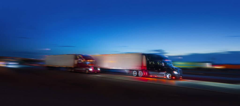 Two commercial semi trucks driving at a fast speed on the expressway.