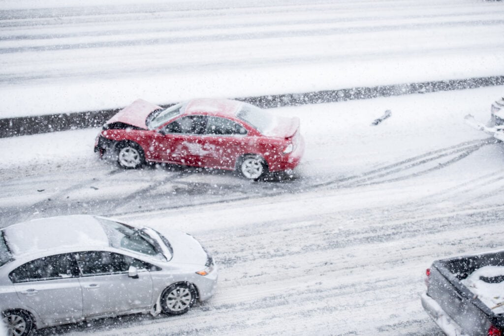 A red car with a damaged front end after an accident in winter conditions on the highway.