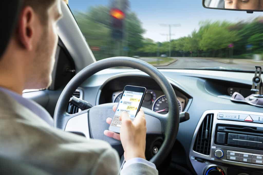 A man is texting on his phone while driving, taking his eyes off of the road and causing a potential fatal situation.