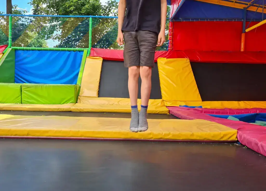 A child wearing striped socks jumps on a trampoline inside a trampoline park.