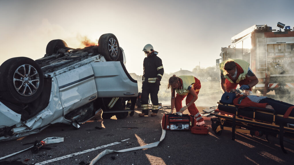 Emergency personnel attend to victims over an accident in which a white SUV rolled over and came to rest on its hood.