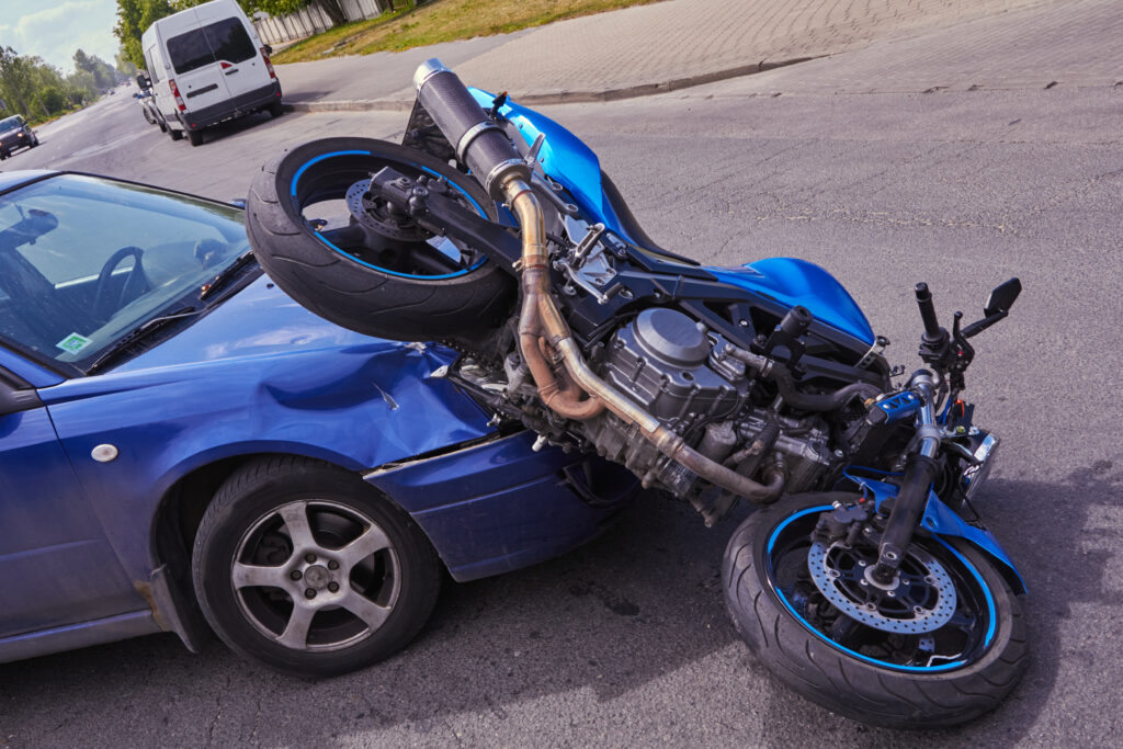 A blue motorcycle turned over on the hood of a blue car after an accident in an intersection.