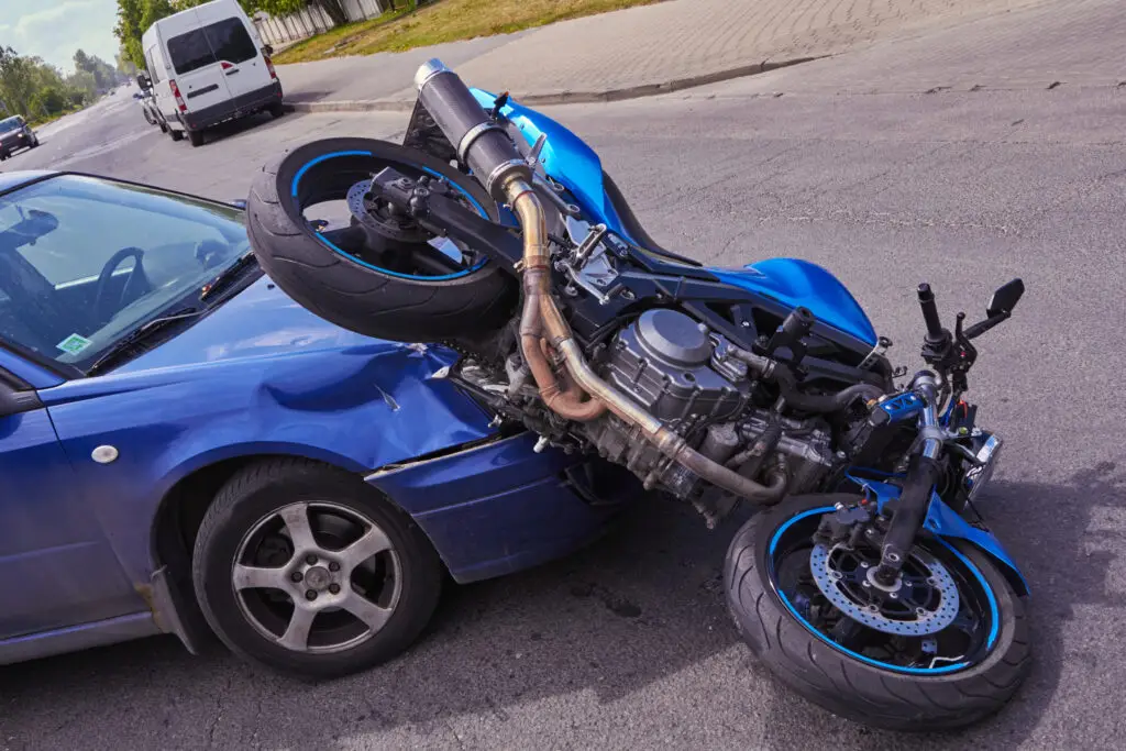 A blue motorcycle turned over on the hood of a blue car after an accident in an intersection.