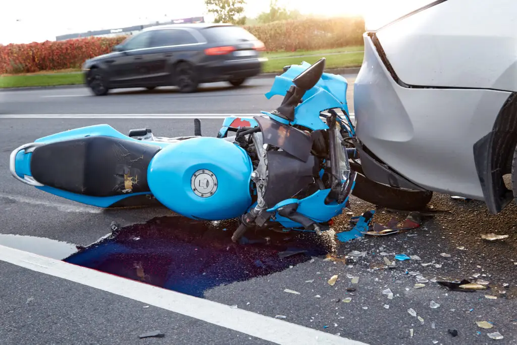 A blue sports motorcycle damaged underneath a car after an accident at high speeds on the highway.