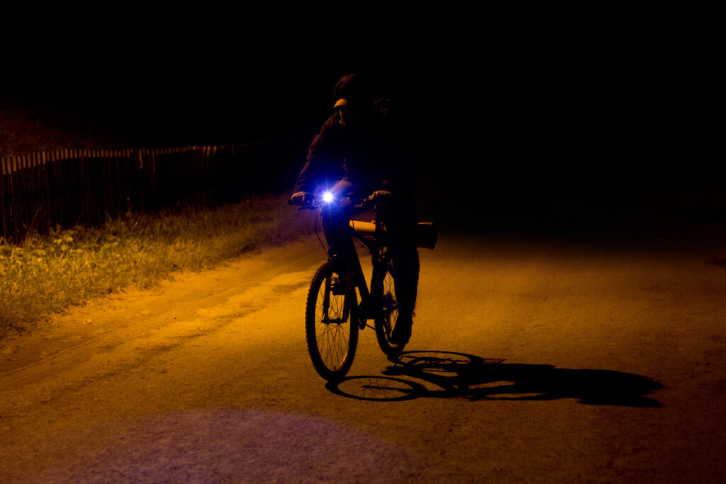 A cyclist riding at night with a headlight on to improve visibility.