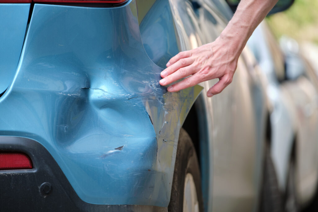 A person inspects the damage to their bumper after being struck by a hit-and-run driver.