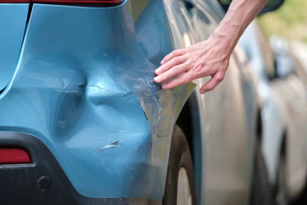 A person inspects the damage to their bumper after being struck by a hit-and-run driver. 