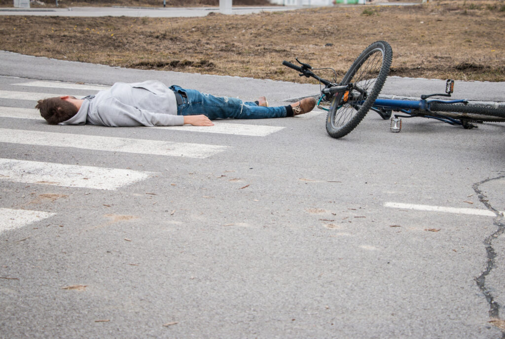 A man is on his back and injured next to his e-bike after an accident with a motor vehicle in a crosswalk.
